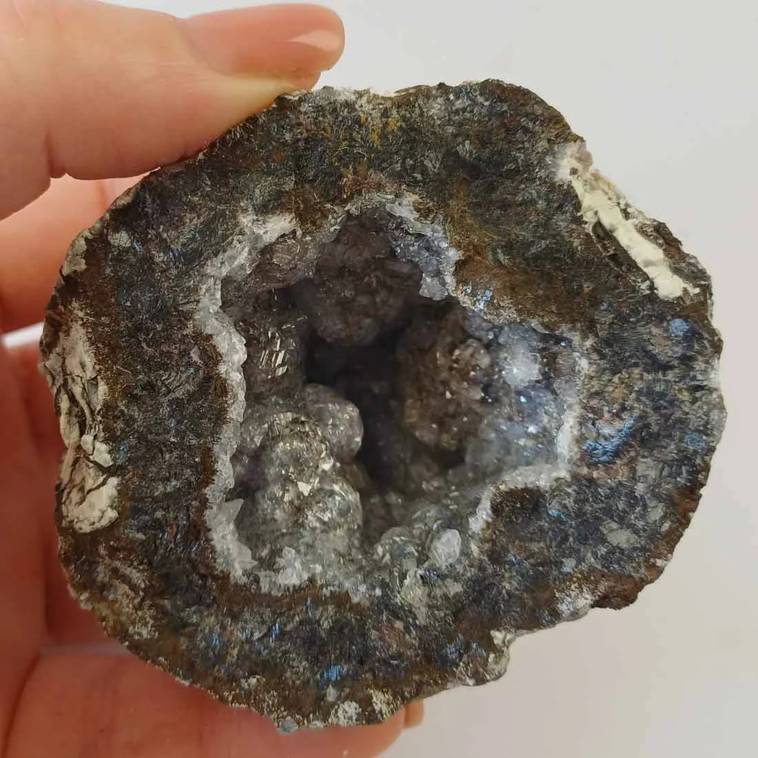 Natural agate geode from Mexico with banded exterior and druzy crystal interior in grey and translucent tones.