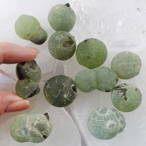 Prehnite with Epidote natural rough crystal showing green botryoidal formations with dark inclusions on white background