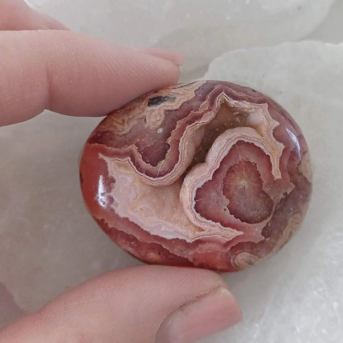 Polished Rhodochrosite palm stone with natural pink, cream, and red banded patterns